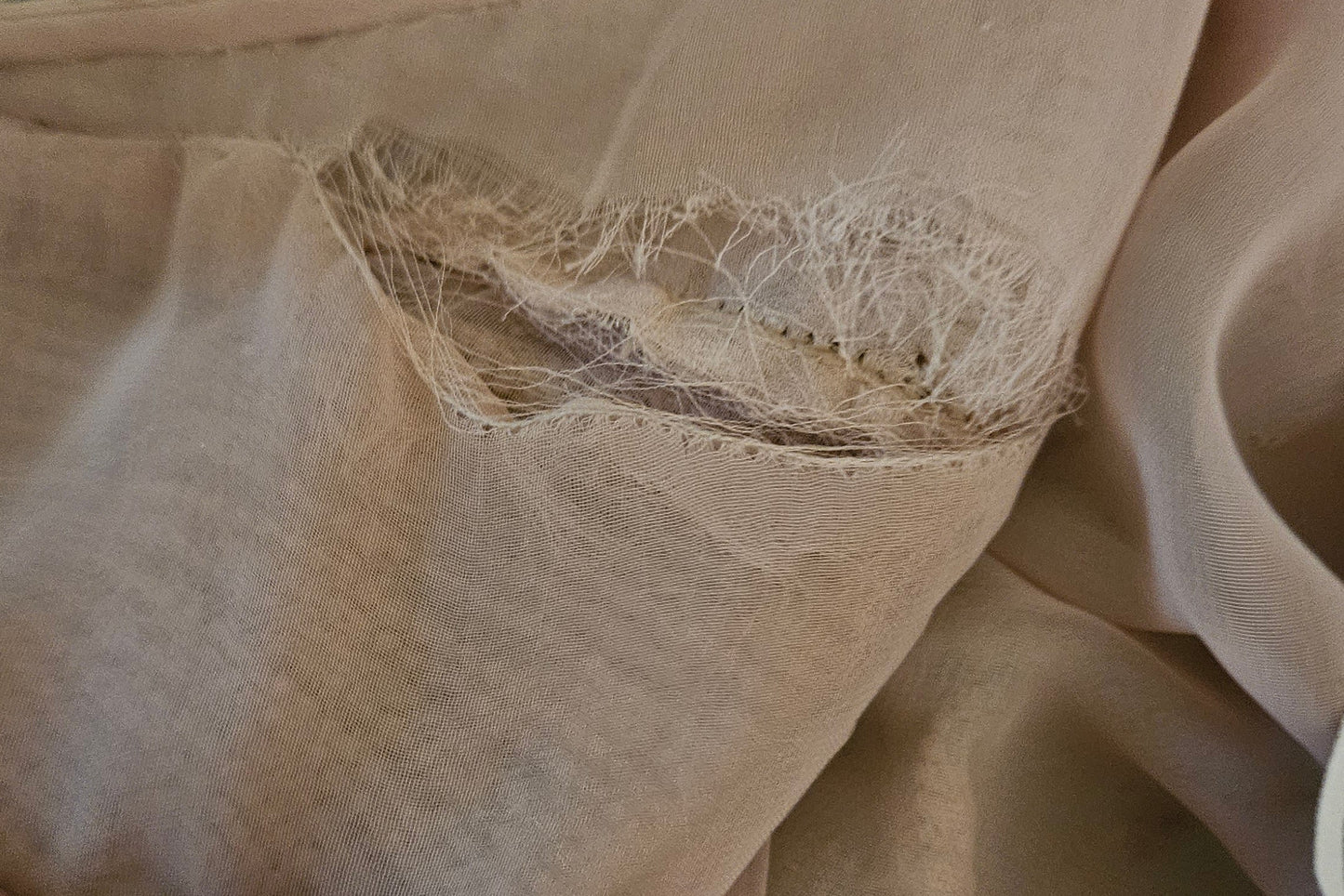 Close-up of beige fabric with a visible tear.