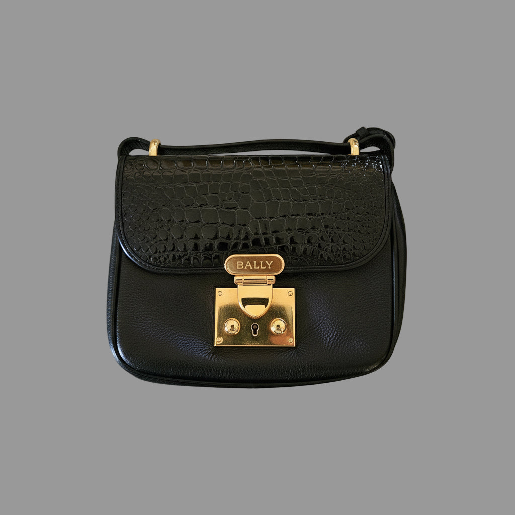 Black handbag with gold clasp on a reflective surface