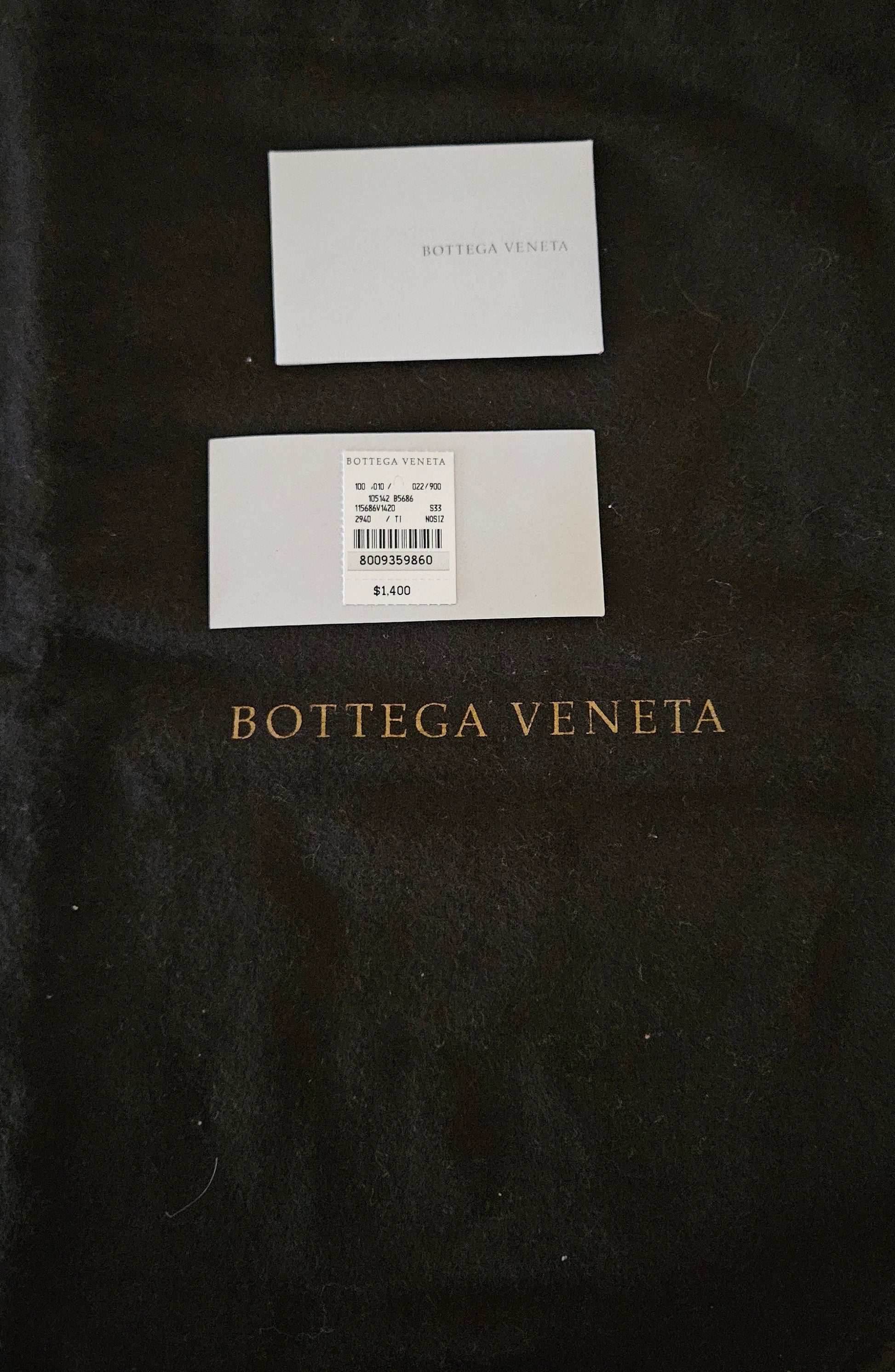 Two white cards on a black dust bag with 'Bottega Veneta' branding.