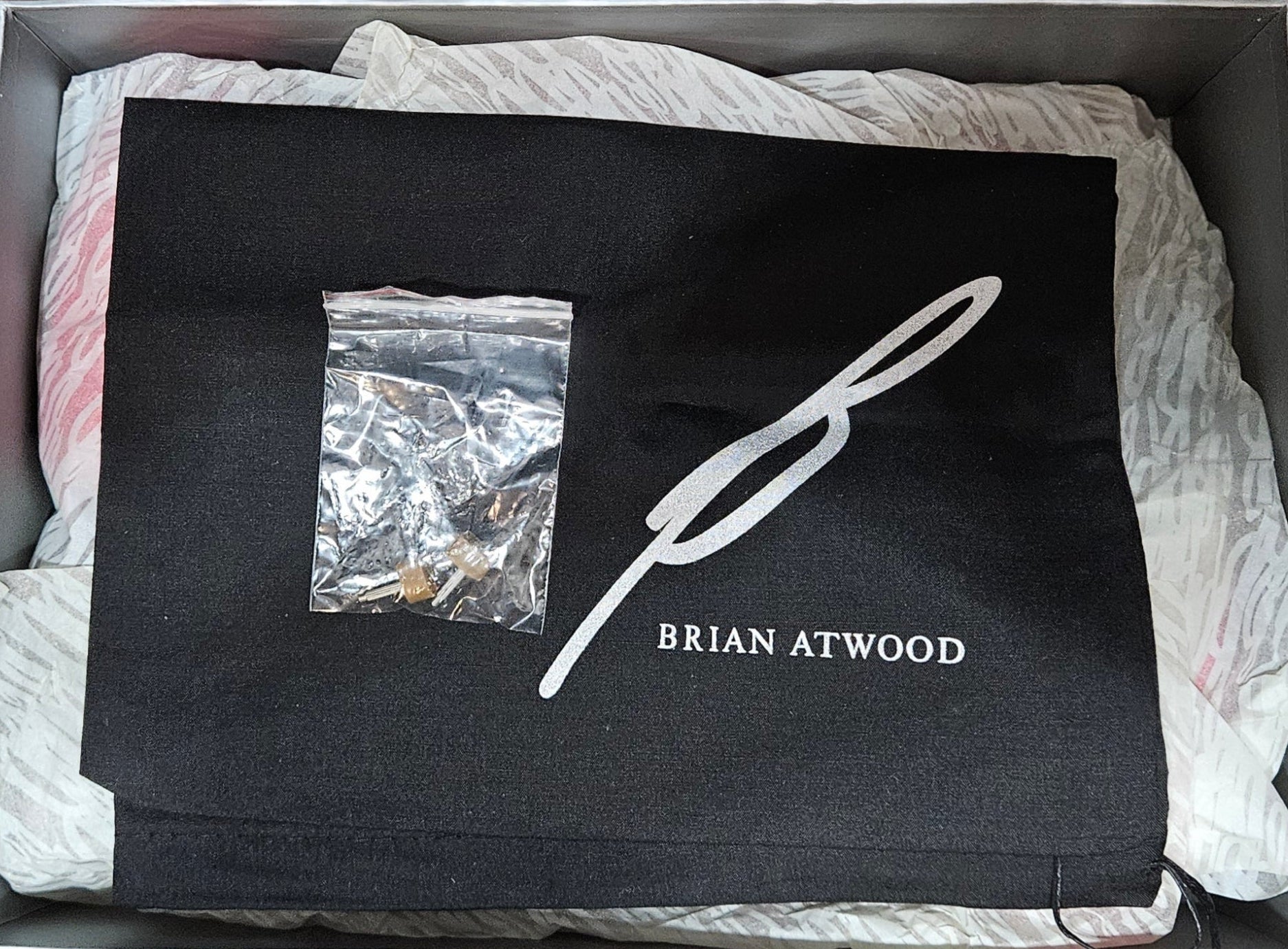 Box containing a black garment with 'Brian Atwood' branding on a wooden surface.