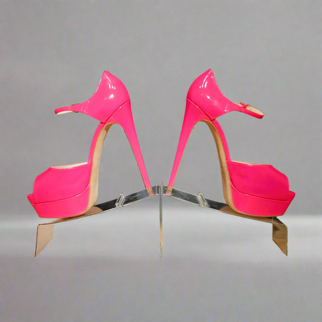 Pair of bright pink high-heeled shoes on a reflective stand against a gray background