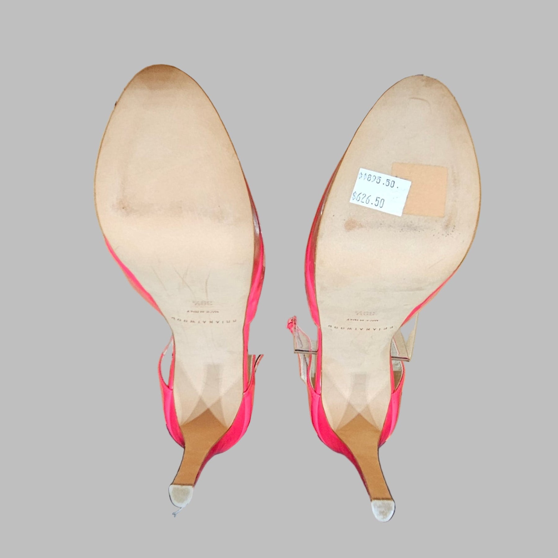 Pair of pink high-heeled shoes on clear stands with a visible brand label.