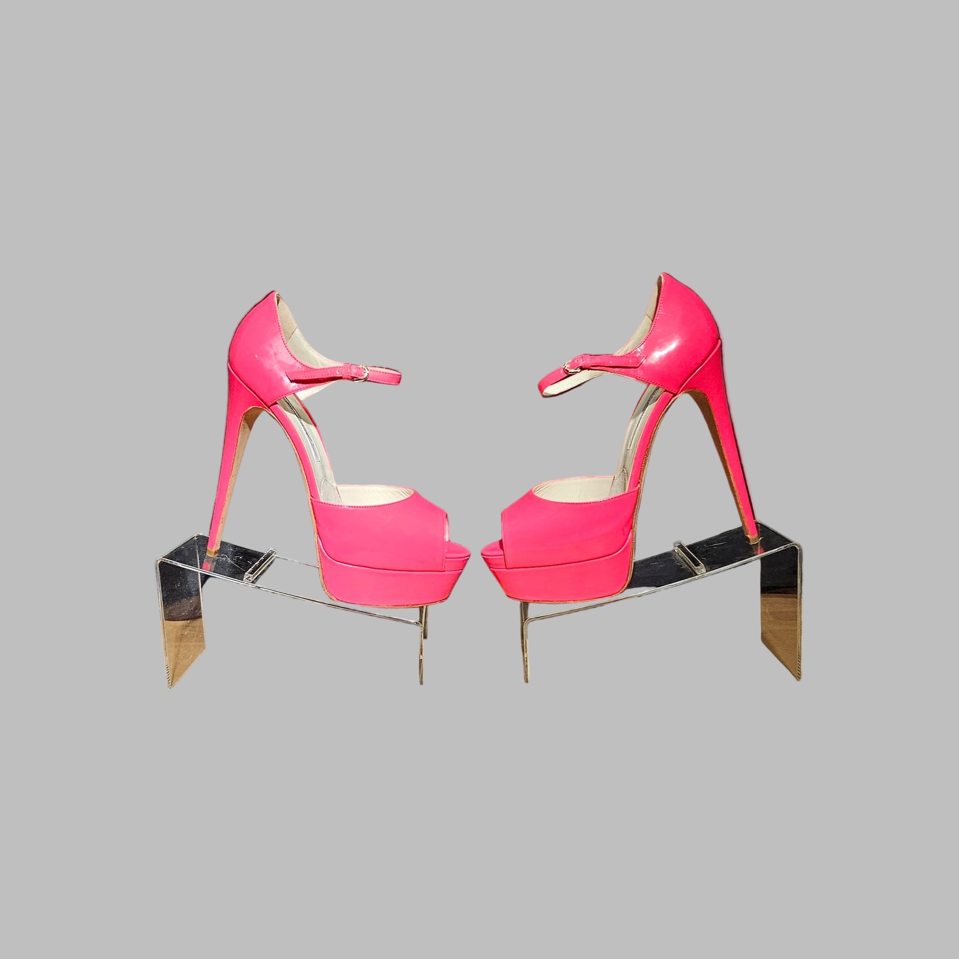Pair of pink high-heeled shoes on a reflective stand against a gray background