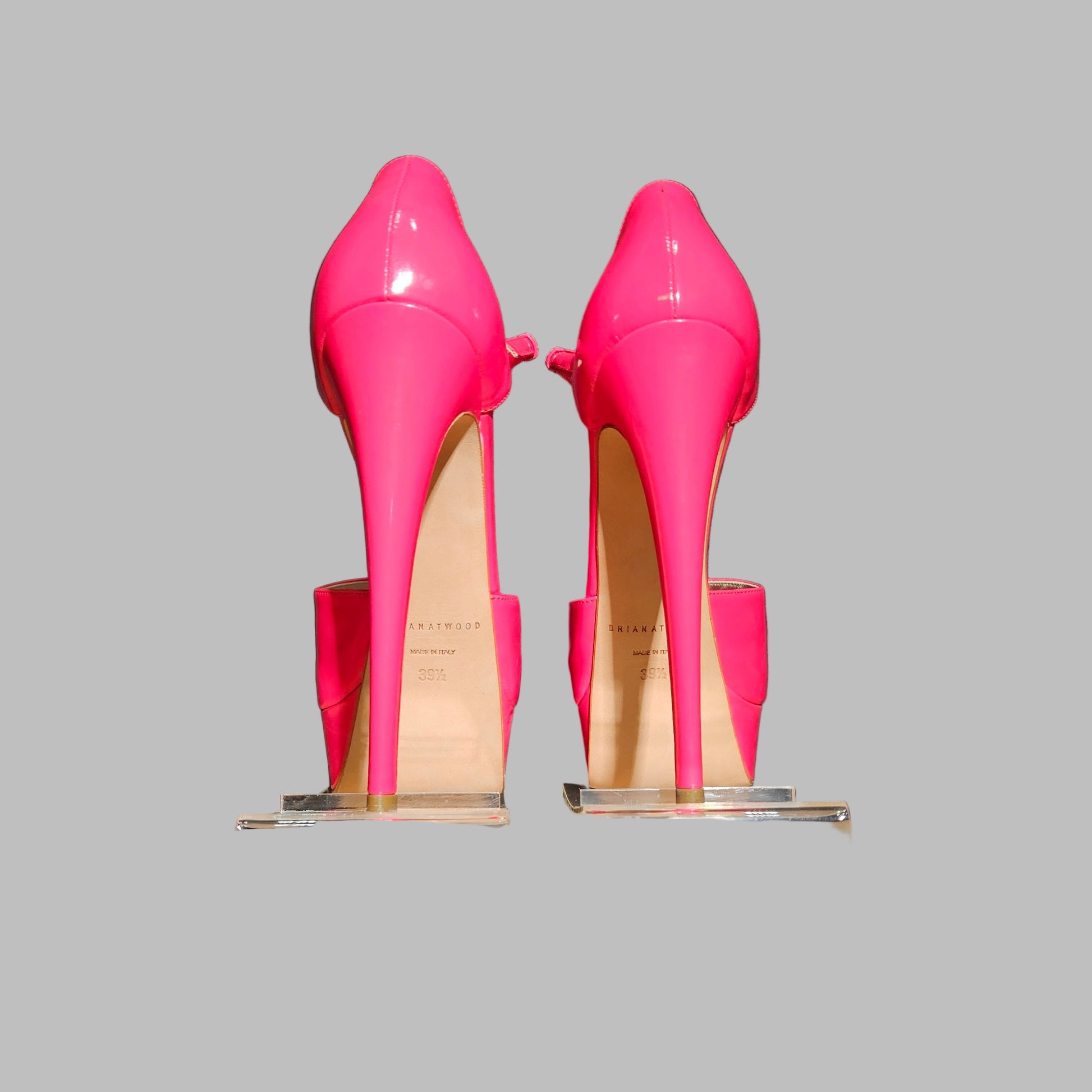 Pair of bright pink high-heeled shoes on clear stands against a dark background