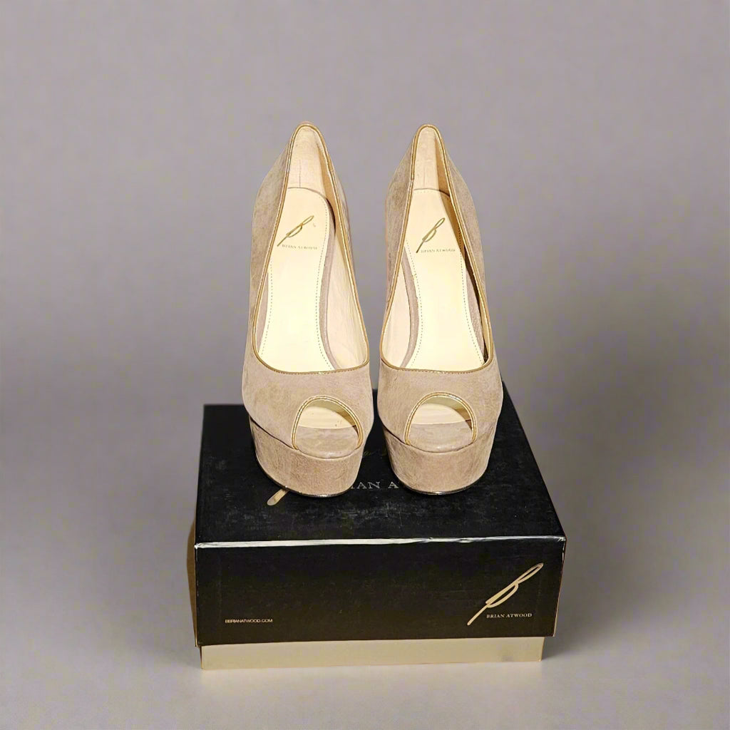 Taupe high-heeled shoes on a black box with a cardboard box underneath against a dark background