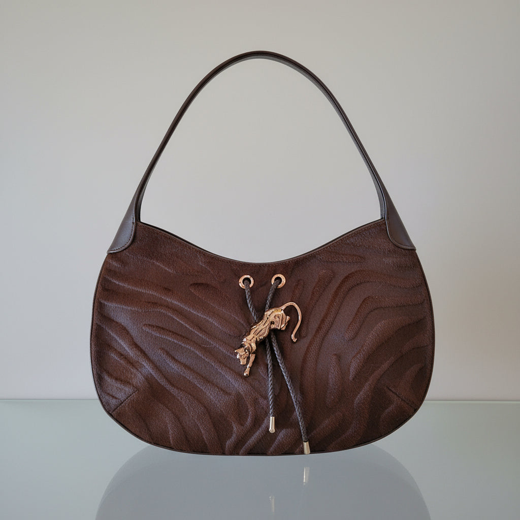 Brown textured handbag with a drawstring on a reflective surface and panther charm