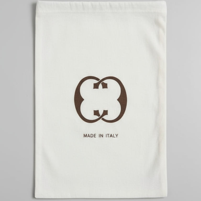 Brown leather bag on a glass table with a white pouch featuring a logo.