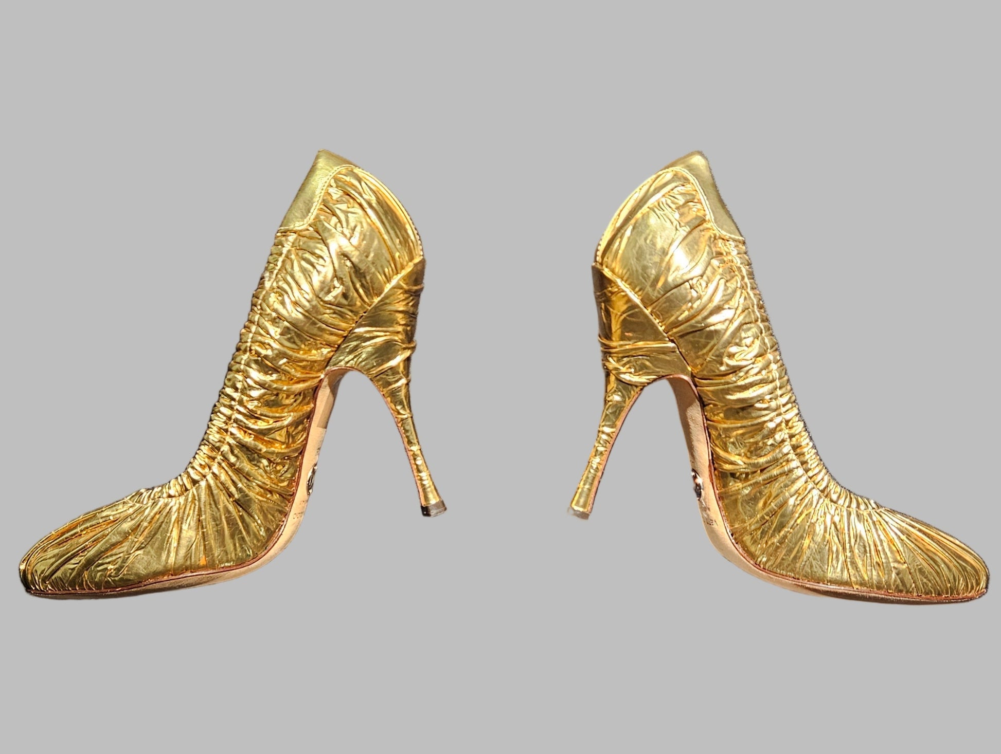 Gold high-heeled shoes on a clear stand against a dark background