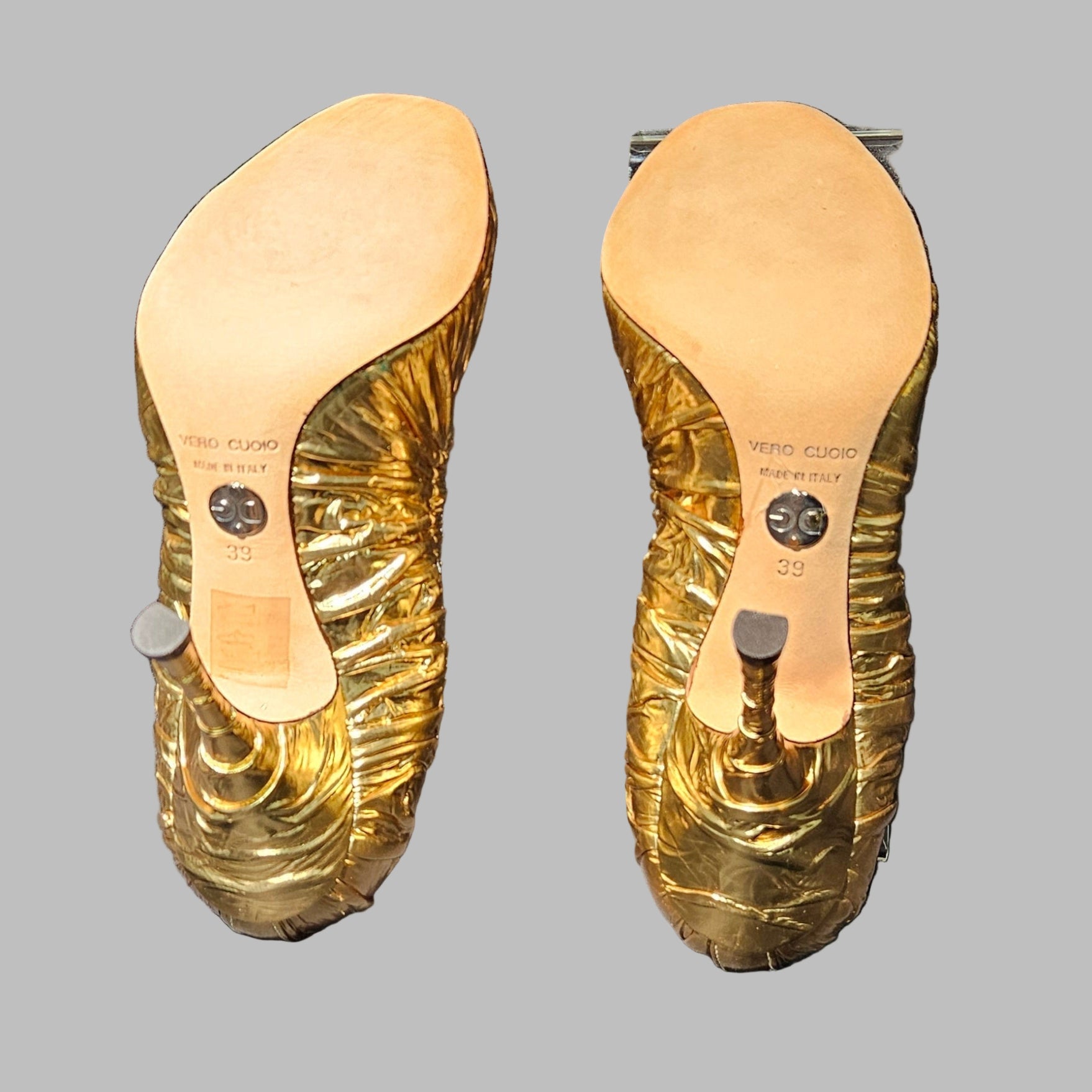 Gold high-heeled shoes with visible brand name on a gray background