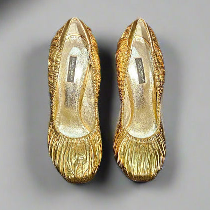 Gold high-heeled shoes on a black stand with 'Dolce & Gabbana' branding against a black background