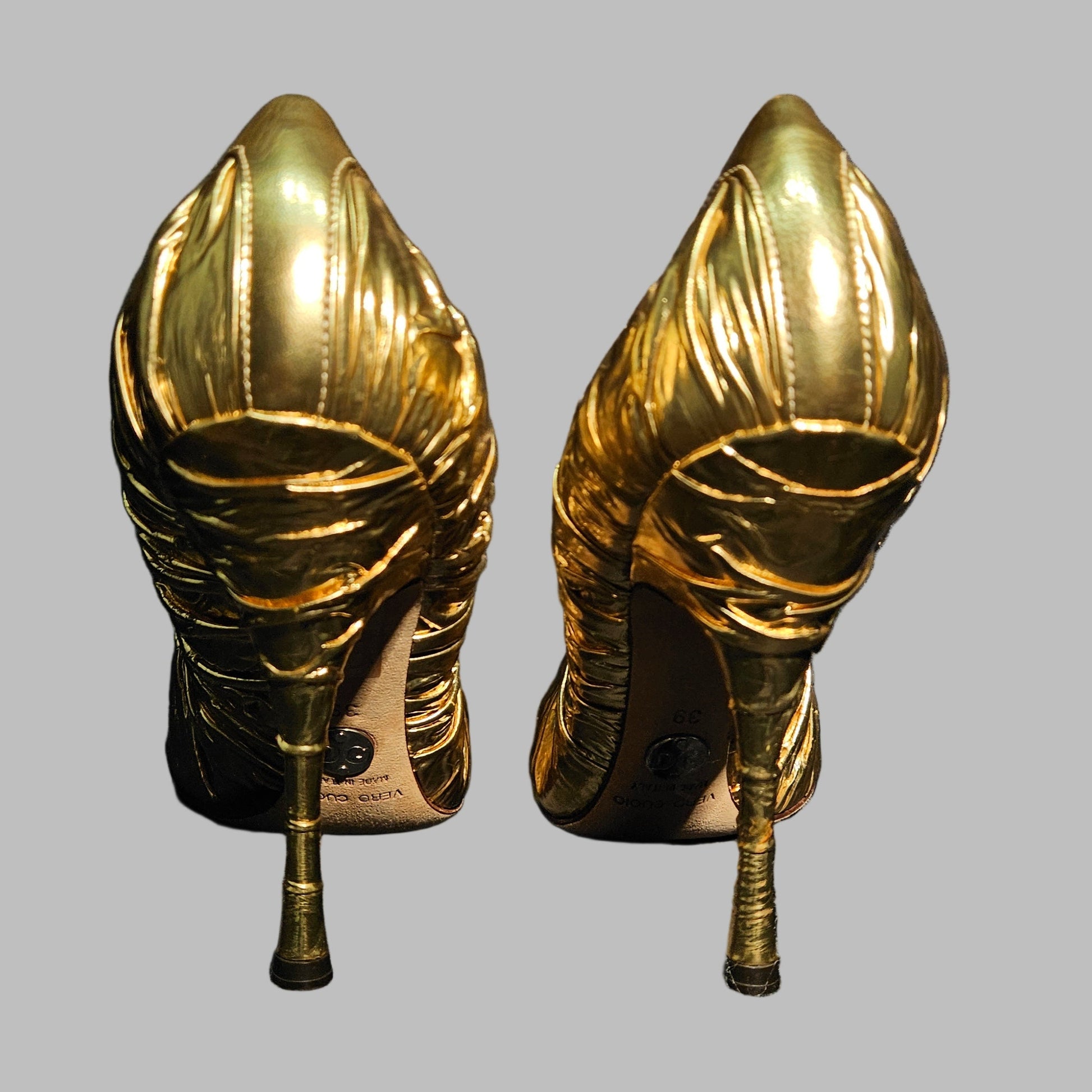 Pair of gold high-heeled shoes on a gray background