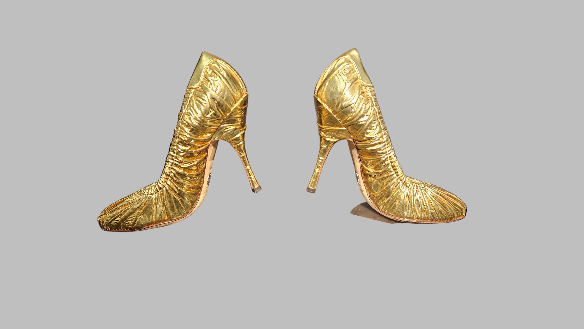 Pair of gold high-heeled shoes on a gray background