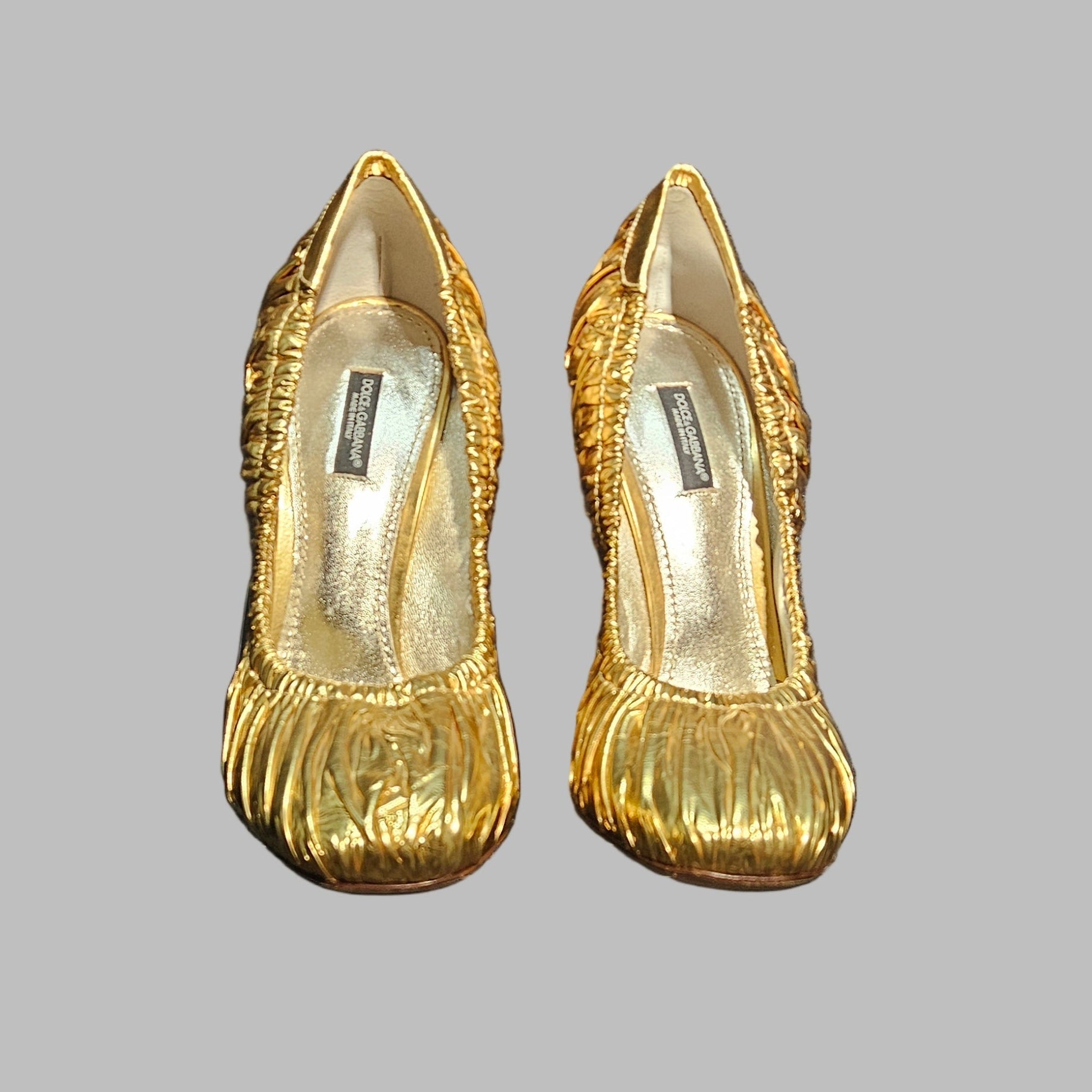Gold high-heeled shoes with a Dolce & Gabbana pouch on a dark background