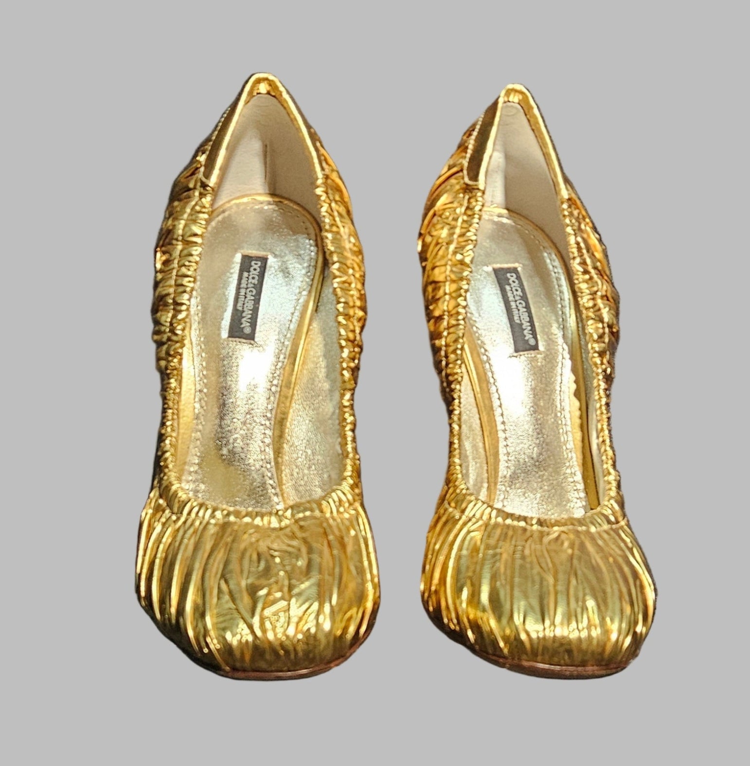 Pair of gold high-heeled shoes on a gray background