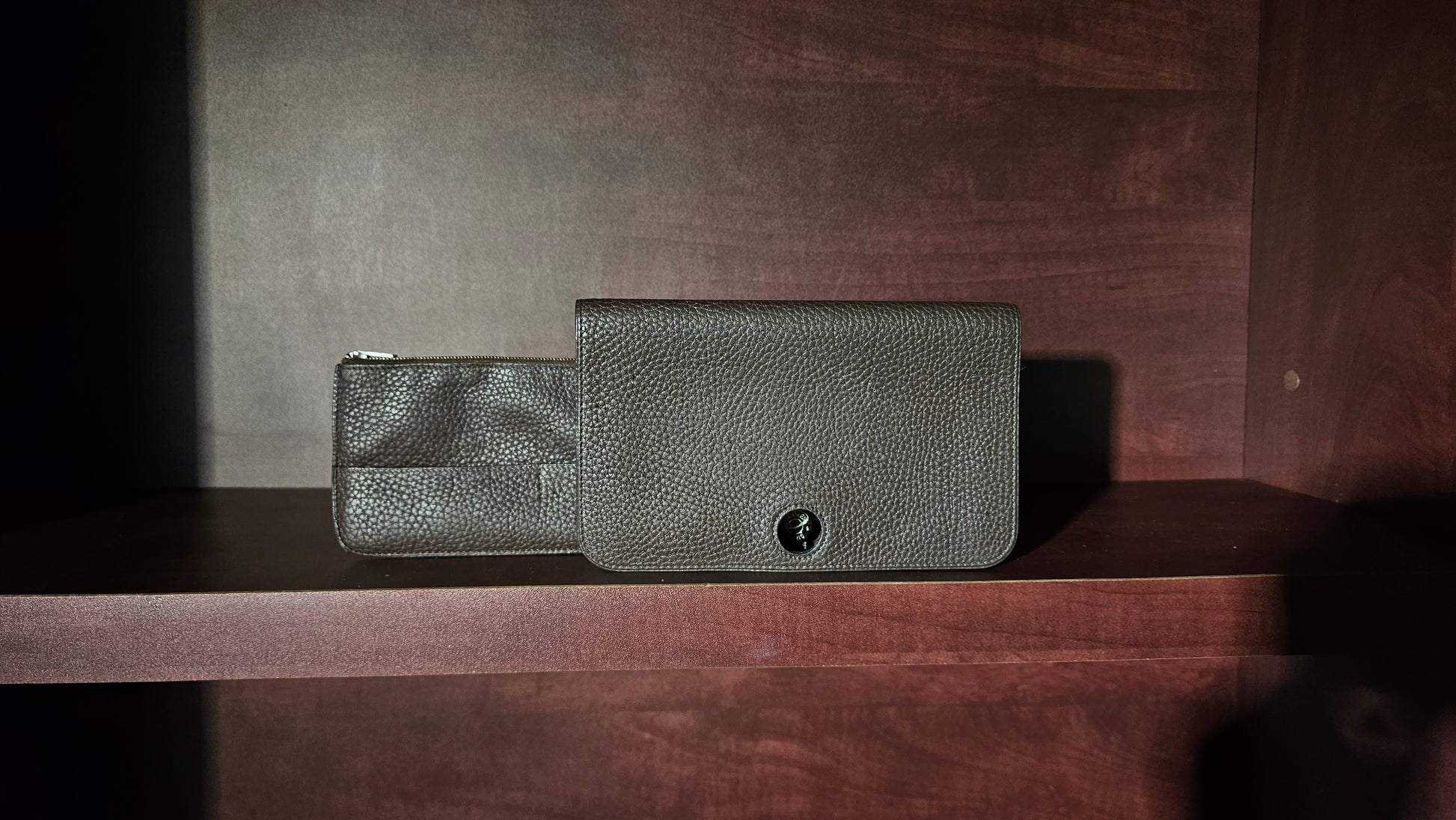 Two dark gray leather wallets on a wooden surface with a dark background