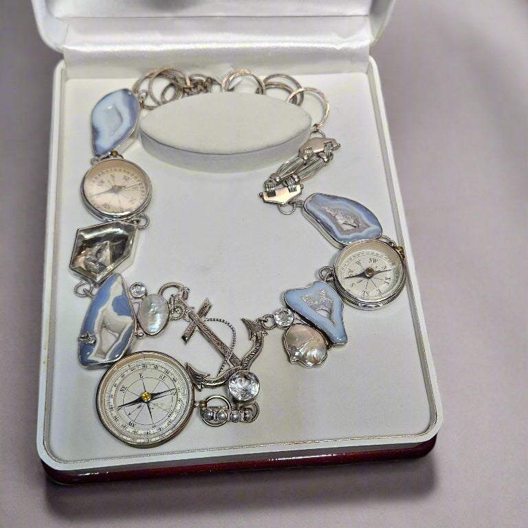 Silver charm bracelet with various charms on a white display box.