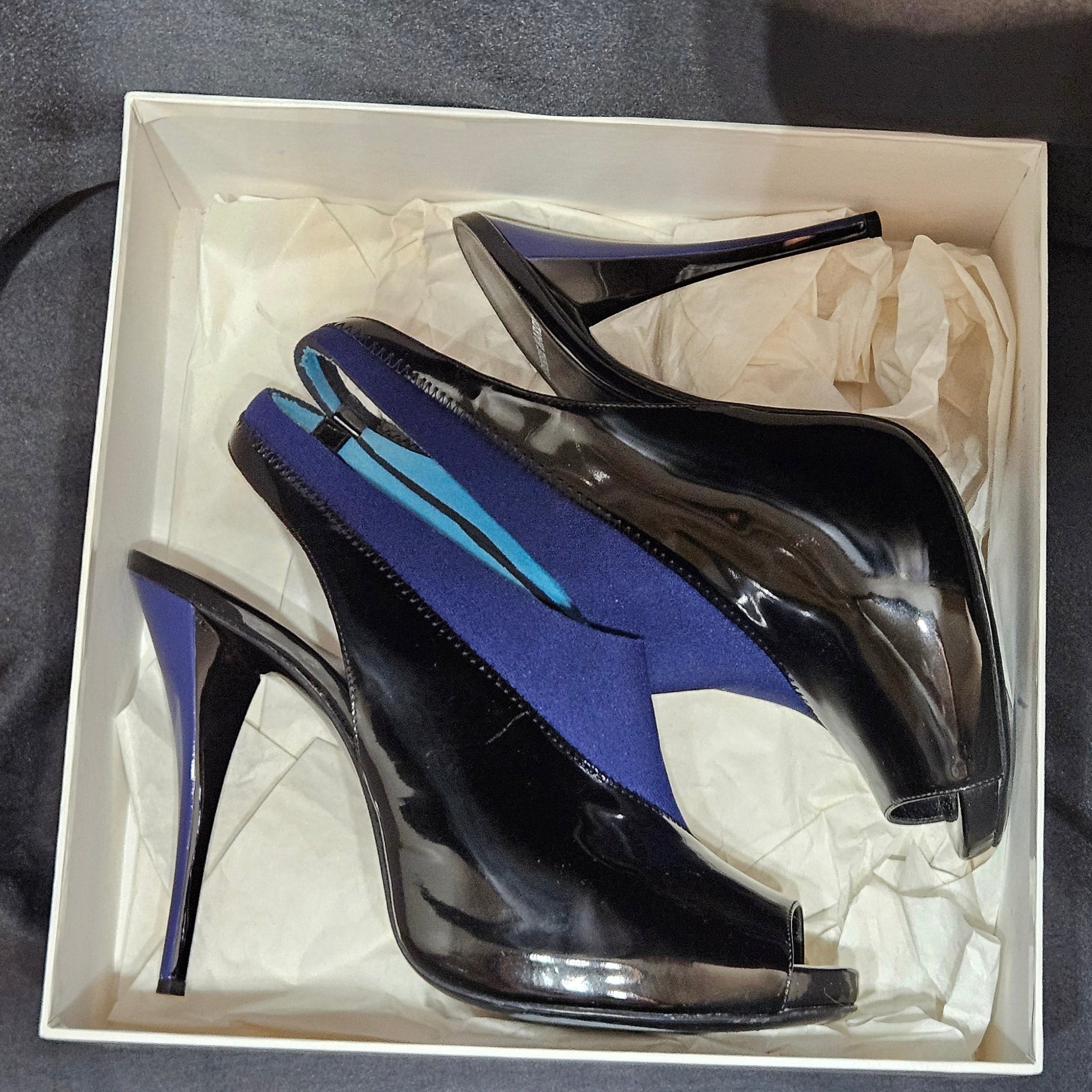 Pair of black and blue high-heeled shoes in a box on a dark fabric background