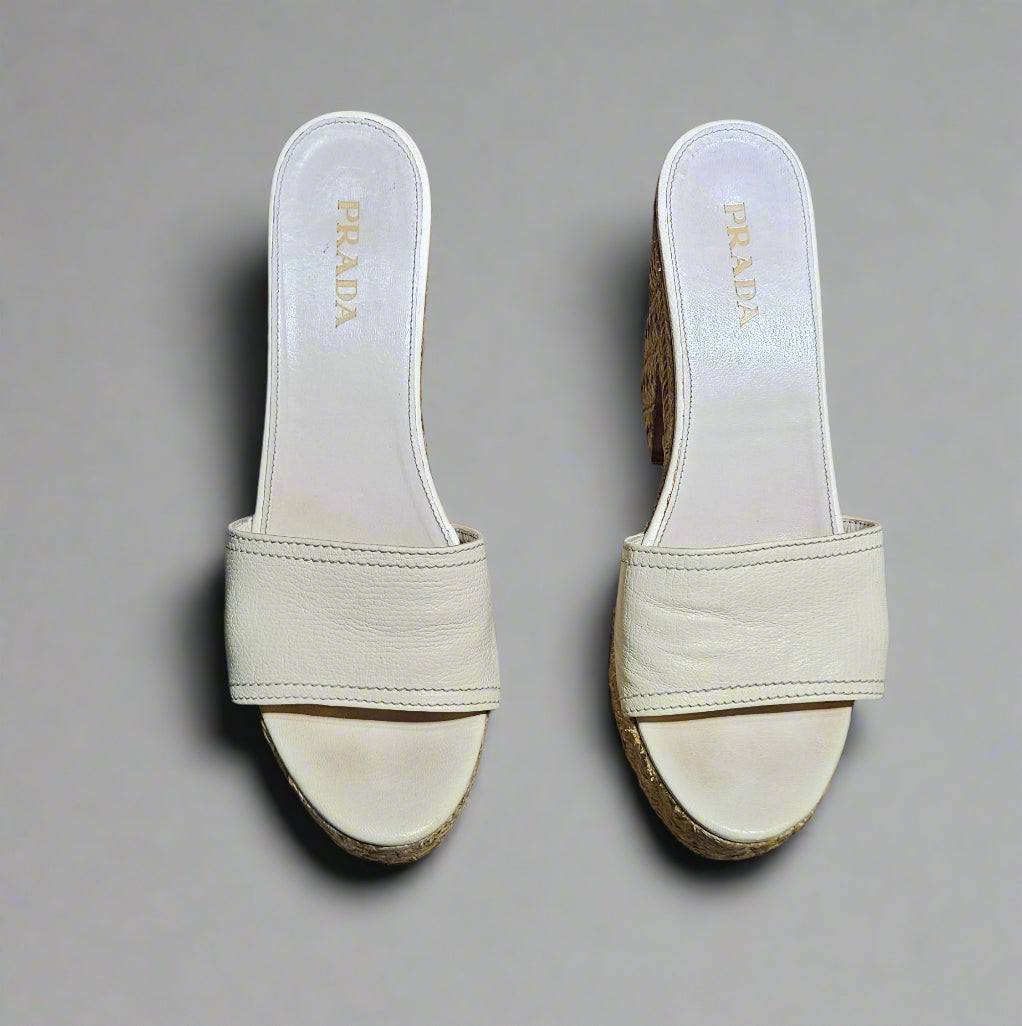 Pair of white Prada sandals on a marble surface with a red background