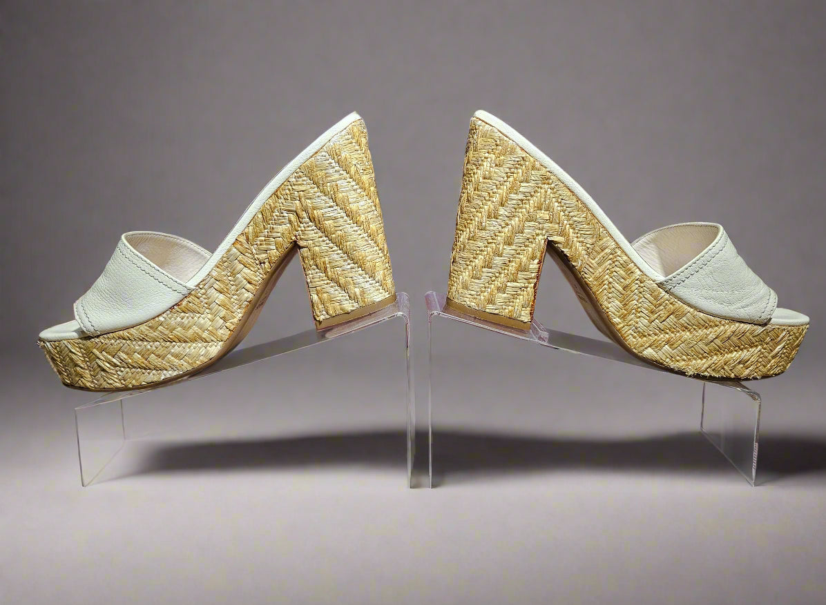 Pair of gold and white high-heeled shoes on a clear stand against a maroon background.