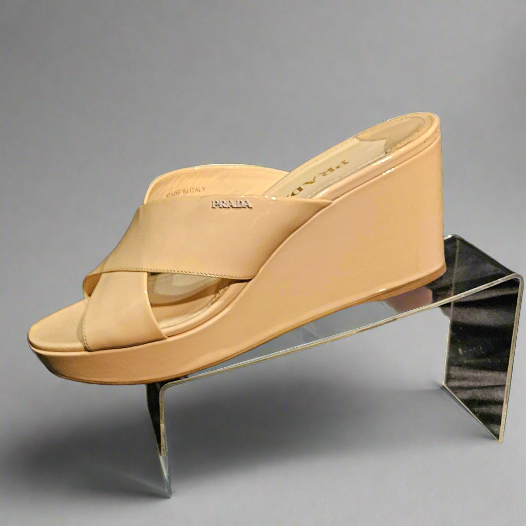 Beige wedge sandal on a clear stand against a dark background
