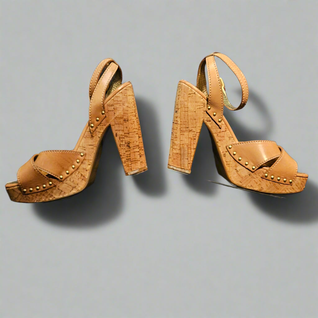 Pair of tan high-heeled shoes on a clear stand against a dark background