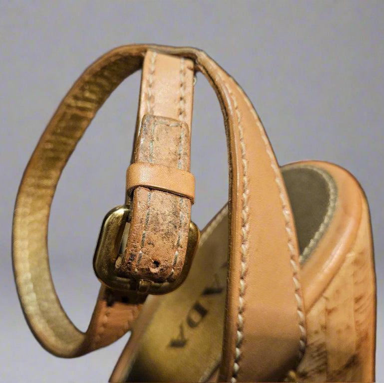 Close-up of a brown leather sandal with a strap and buckle on a gray background