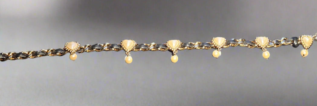 Gold chain belt with heart-shaped charms and small beads on a gray background