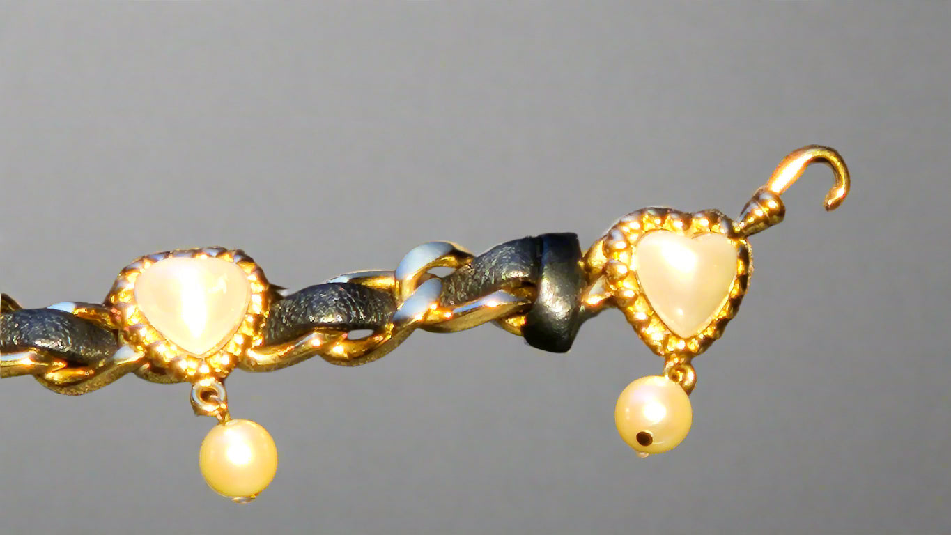 Gold bracelet with heart-shaped charms and pearls on a gray background