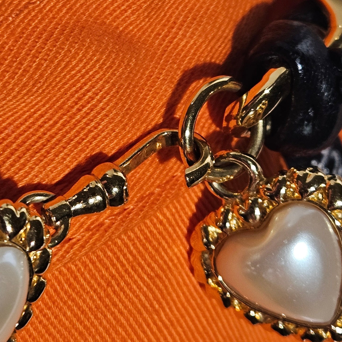 Gold belt with heart-shaped pearl charm on an orange fabric background
