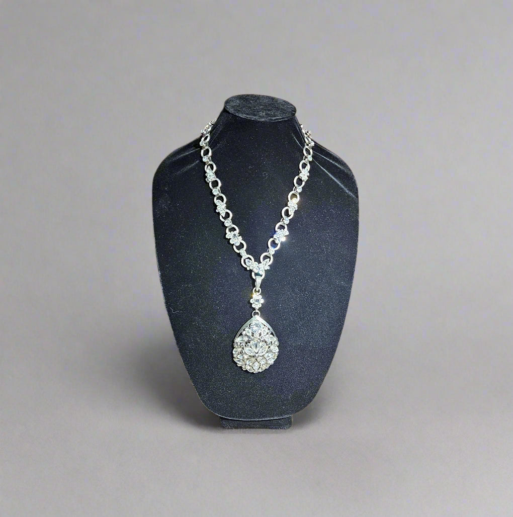 Silver necklace with a pendant on a black stand against a wooden background