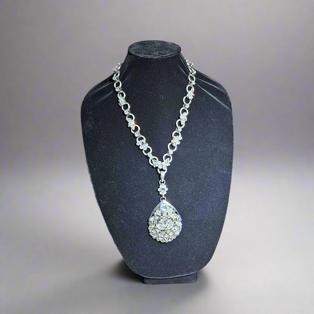 Silver necklace with a teardrop pendant on a black stand against a wooden background