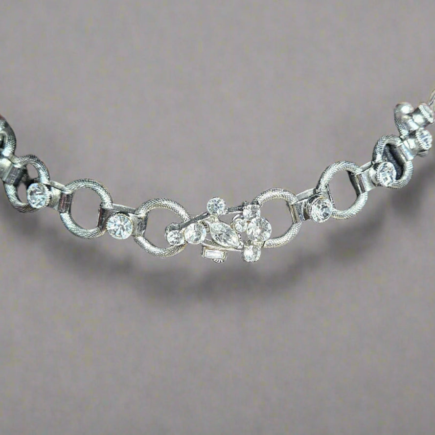 Silver necklace latch with clear stones on a black velvet stand against a blurred background