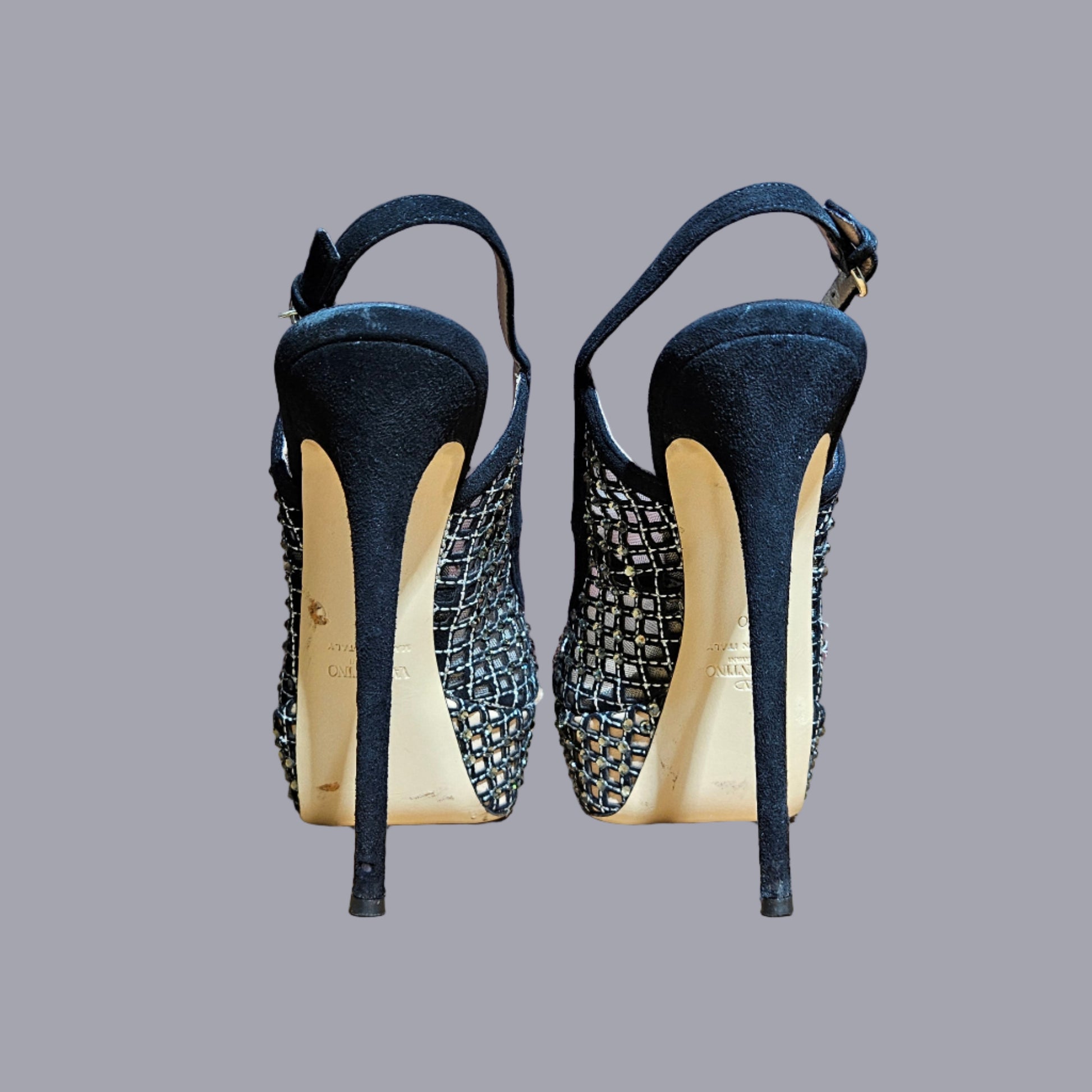 Pair of black high-heeled shoes with textured soles on a gray background