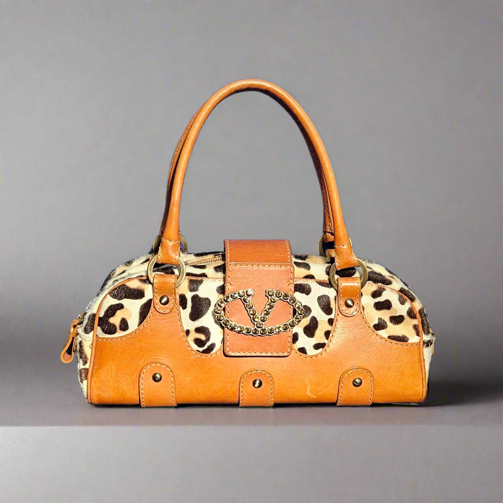 Leopard print handbag with brown leather accents on a gray background
