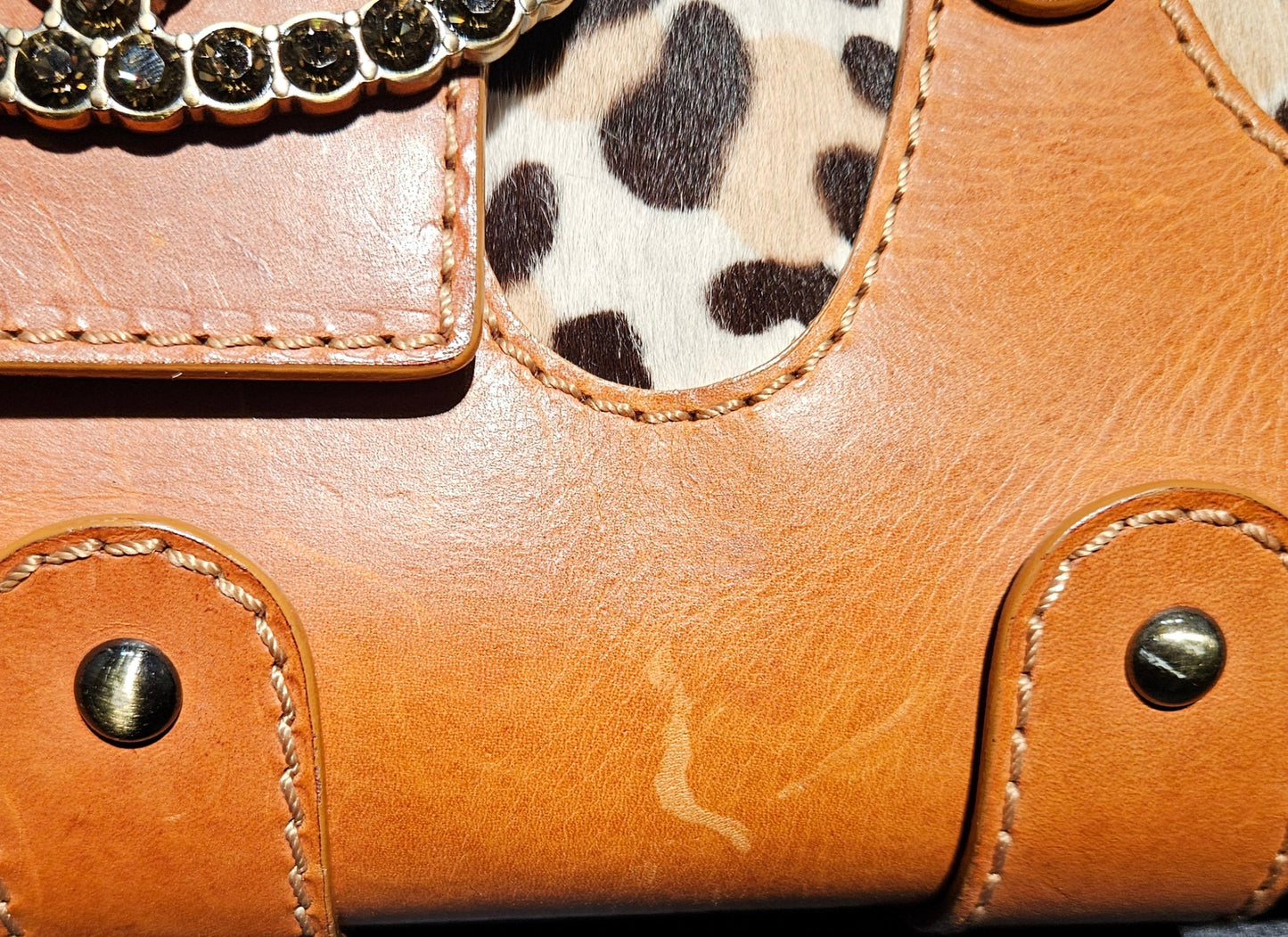 Close-up of a brown leather handbag with leopard print accents on a dark background