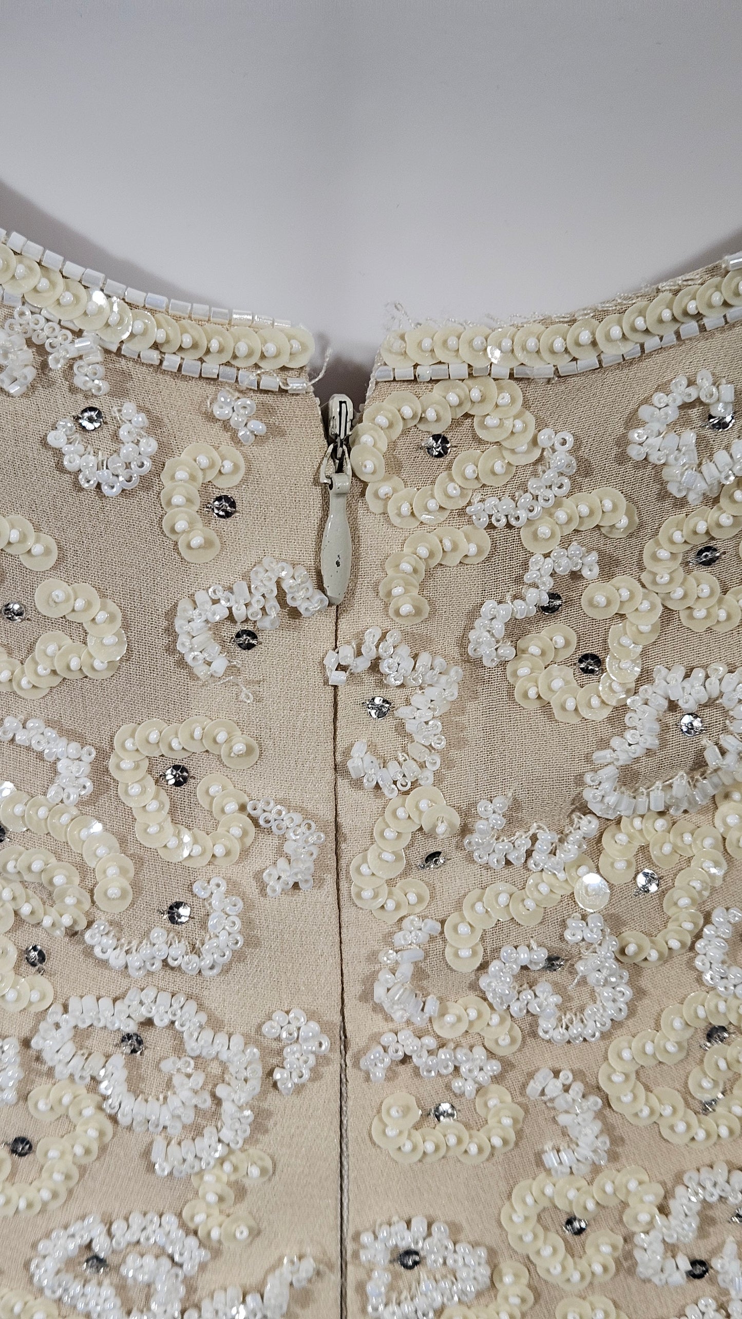 Beige fabric with intricate white lace and bead detailing on a plain background