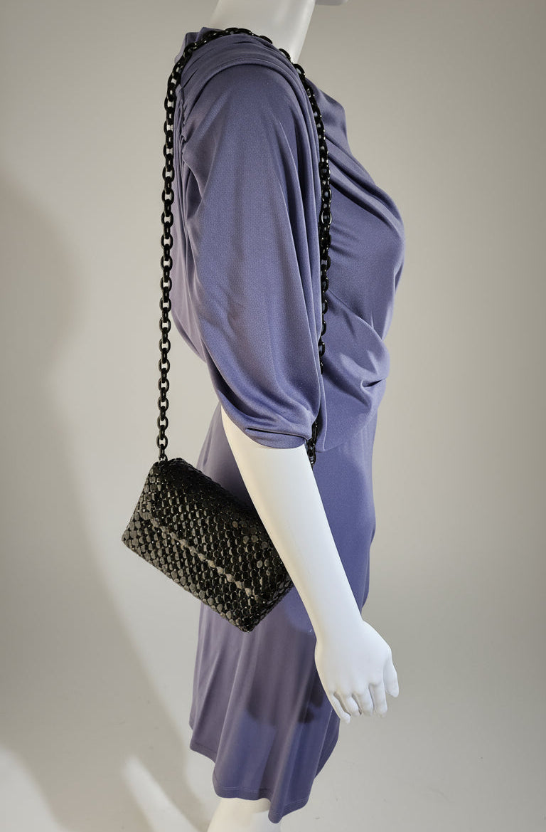 Mannequin wearing a purple dress with a black handbag on a plain background