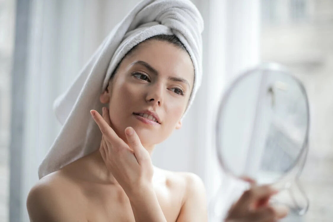 A woman looking in a mirror while applying a skincare product
