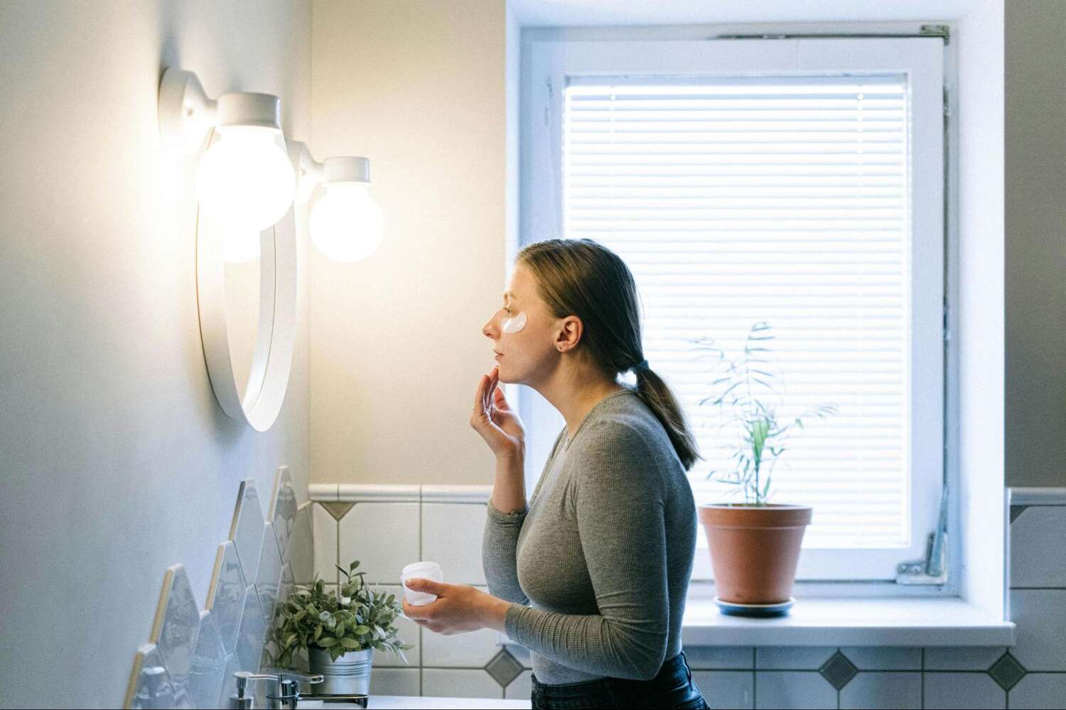 a woman putting on face cream while looking in the mirror