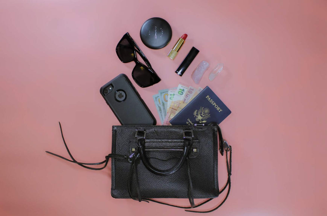 travel essentials in a black purse on a pink background