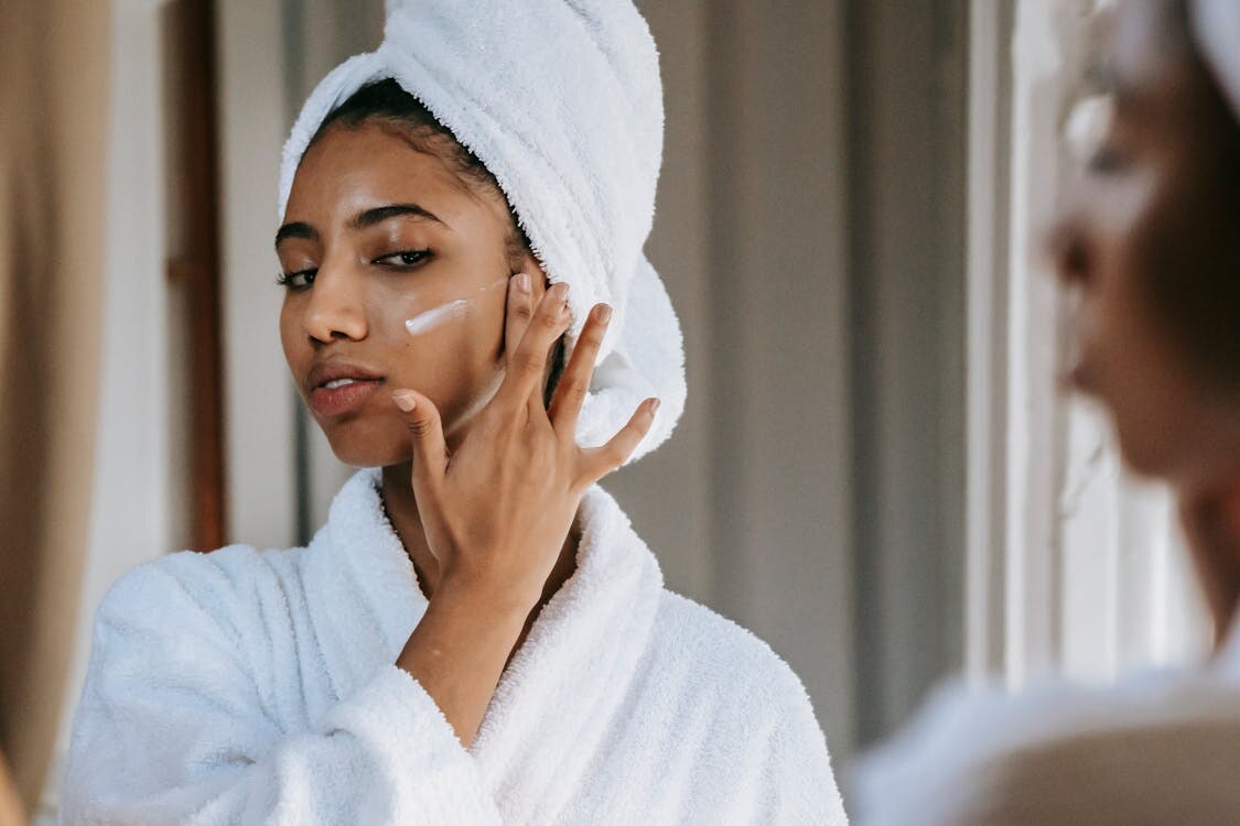 woman applying facial cream in front of a mirror
