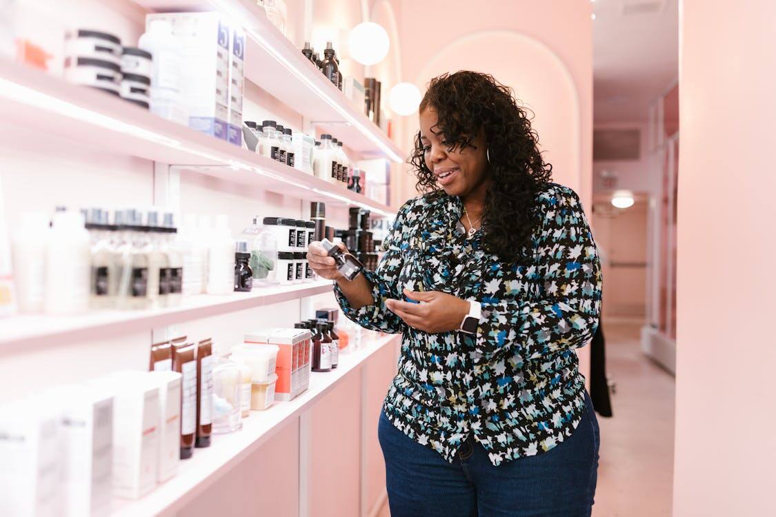 A woman standing in a store aisle reading the label of a skincare product