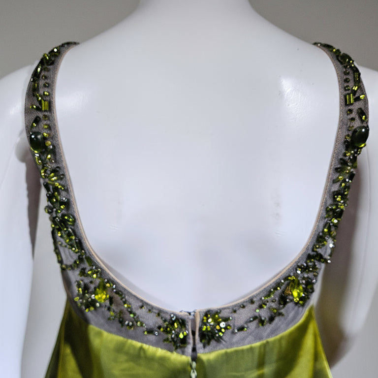 Mannequin wearing a green dress with a beaded back design against a gold curtain background