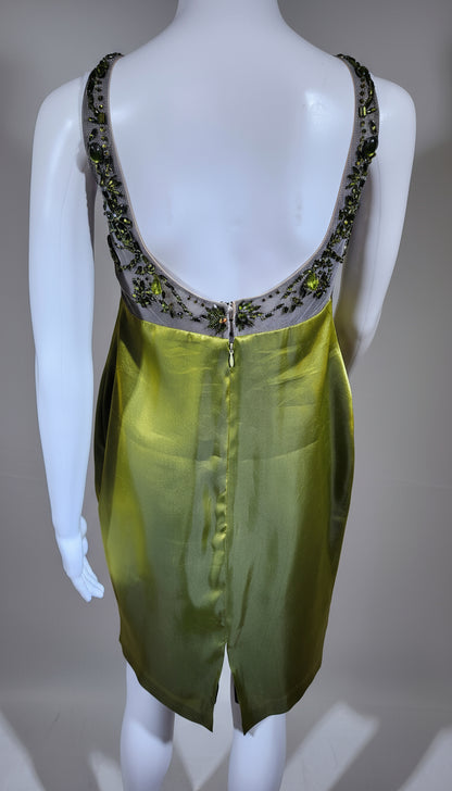 Mannequin wearing a green dress with a black embellished neckline on a wooden floor.