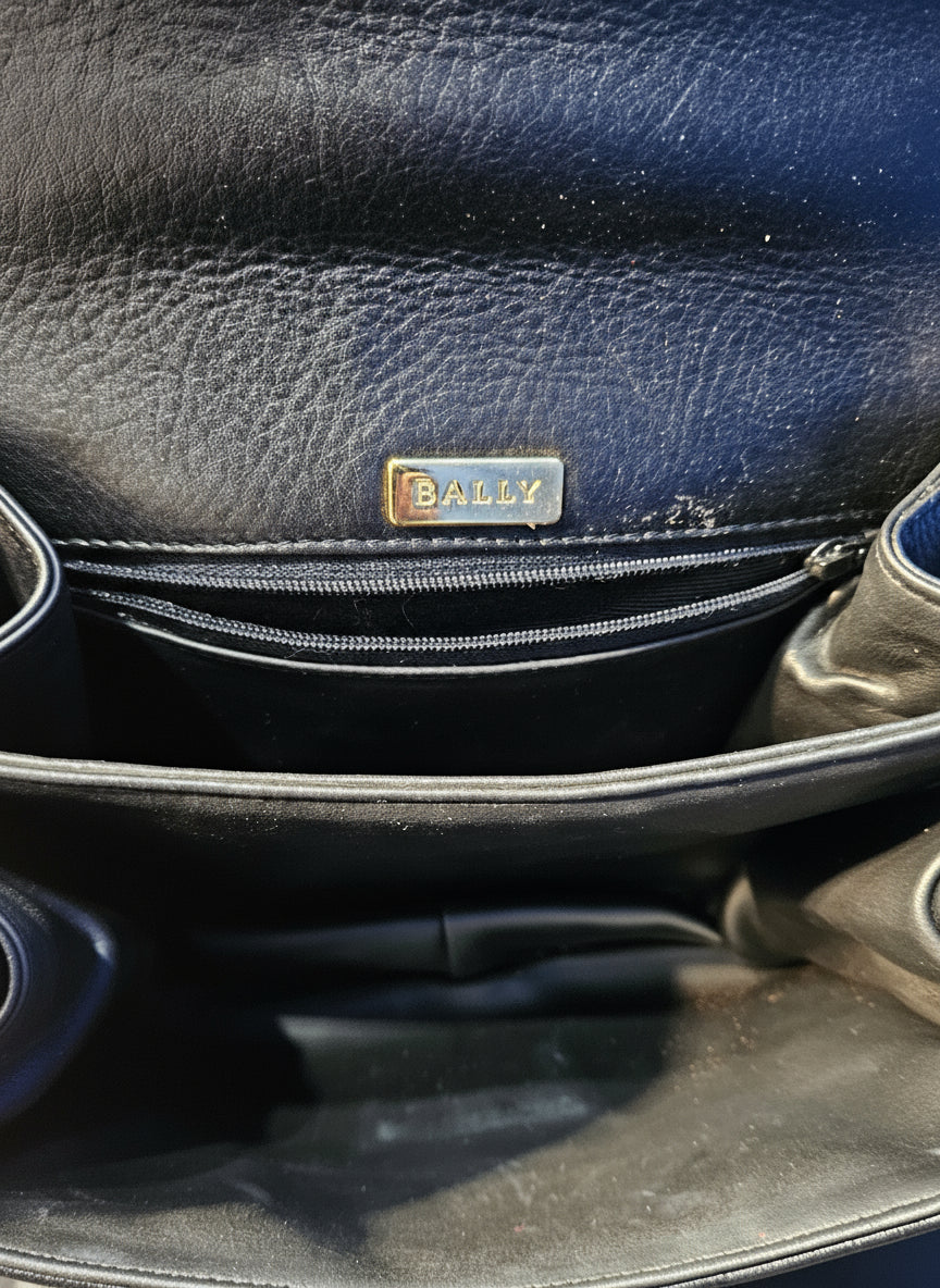 Close-up of a black leather bag with a brand logo on a textured surface.