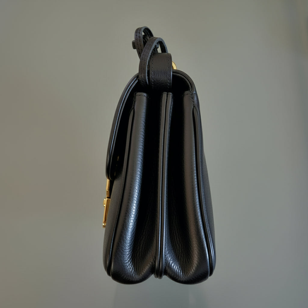 Black leather handbag with gold clasp on a gray background