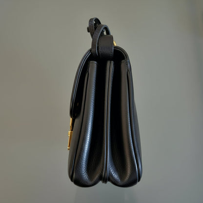 Black leather handbag with gold clasp on a gray background