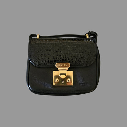 Black handbag with gold clasp on a reflective surface