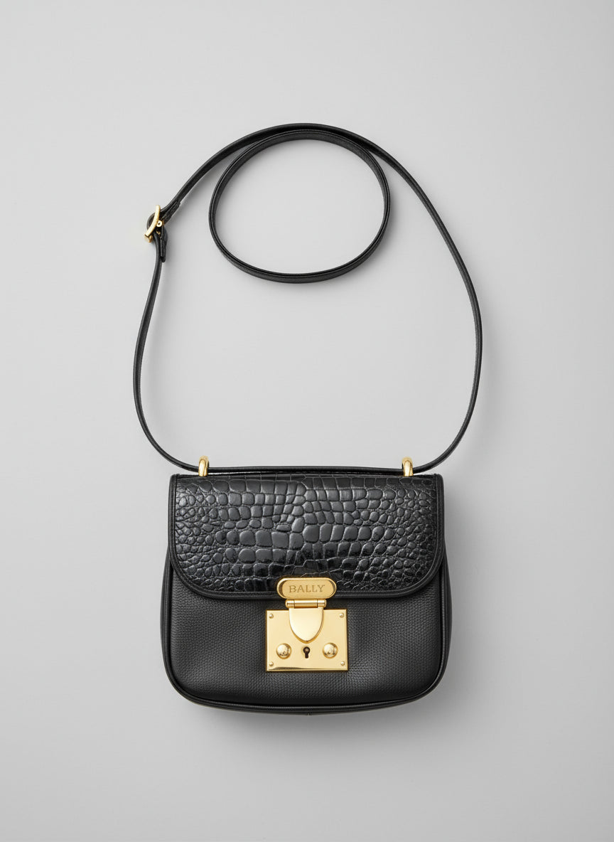 Black handbag with gold clasp on a gray surface