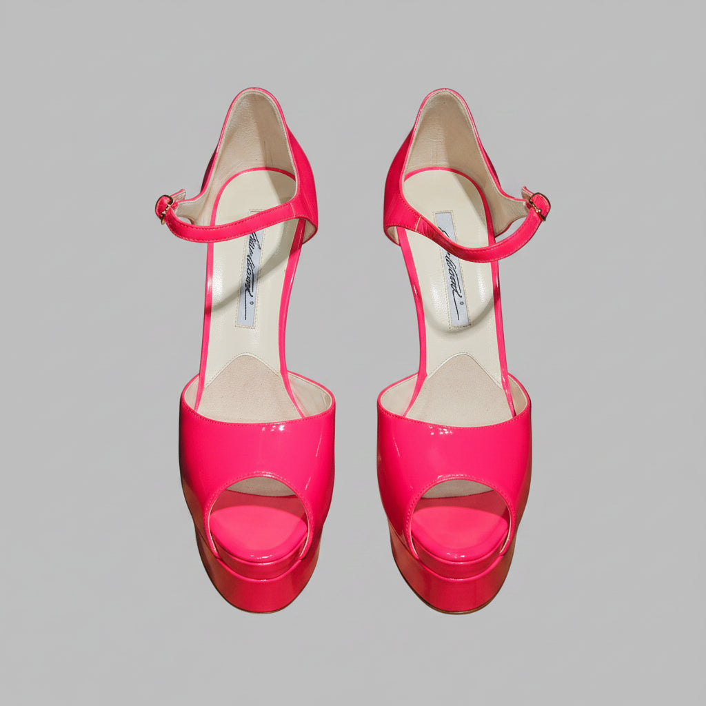 Pair of bright pink high-heeled shoes on a clear stand with a black background